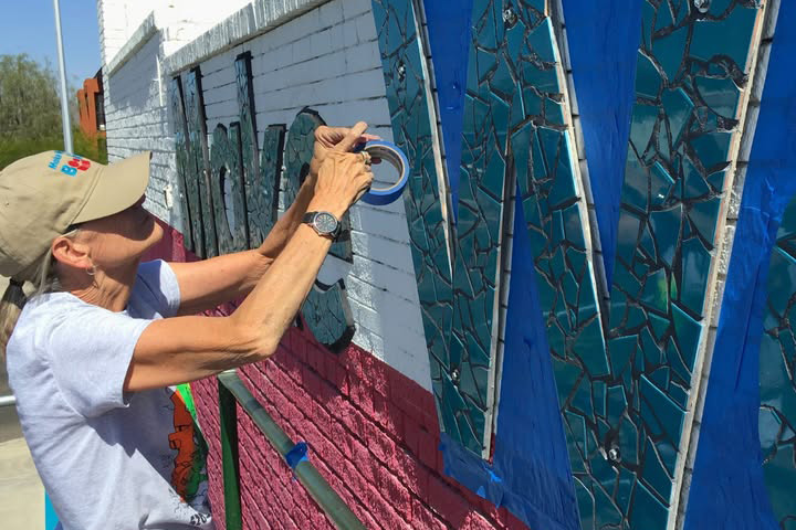 A woman applies blue tape to a Make Way for Books mural