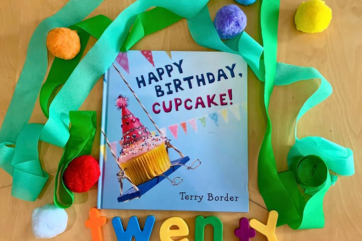 Happy Birthday, Cupcake book surrounded by decorative paper and pompoms