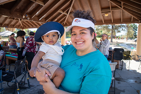 A teen girl in a blue shirt smiles as she holds up her baby