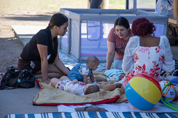 Three teen girls sit on a blanket with their infants
