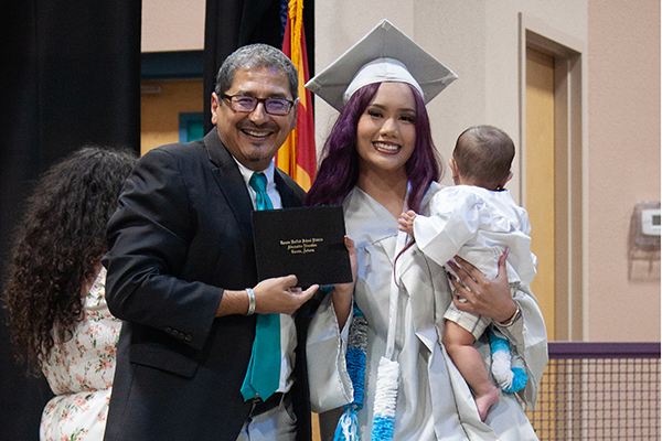 The principal poses with a teen girl graduate and her infant child